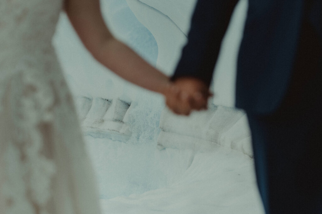 couple hold hands against the backdrop of a glacier waterfall