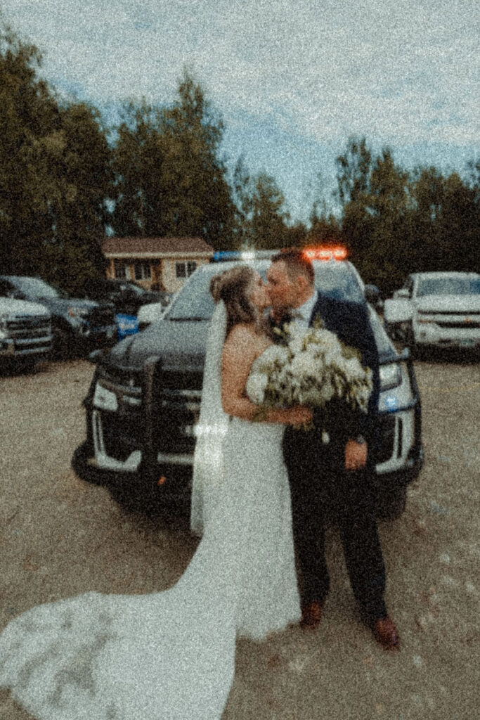 married couple kissing in front of a police car