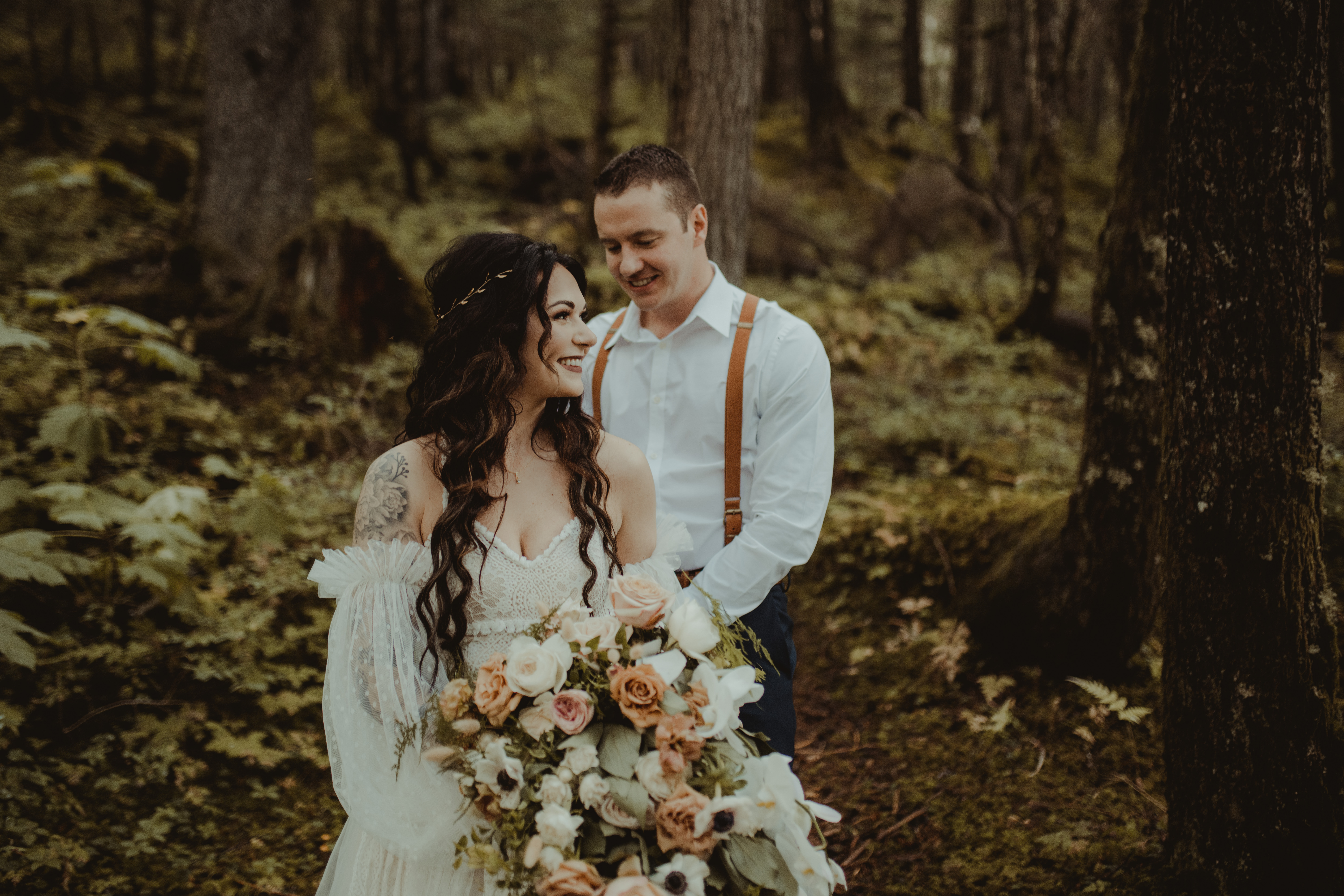 Bride and groom stand in an immense rainforest in alaska