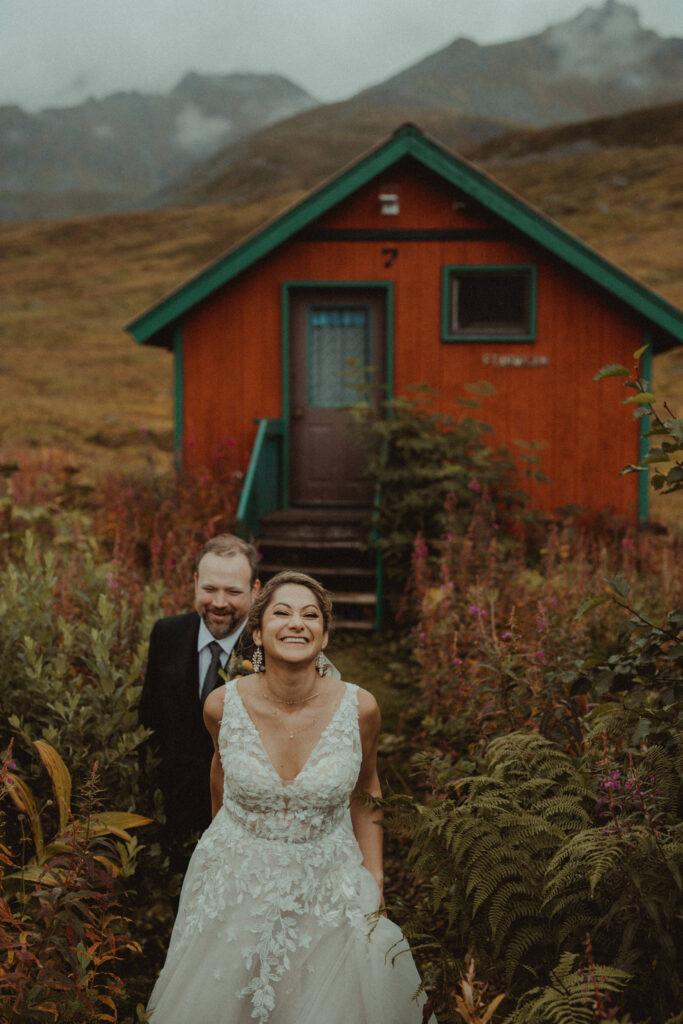 Bride leads the groom away from a cabin in Hatcher Pass