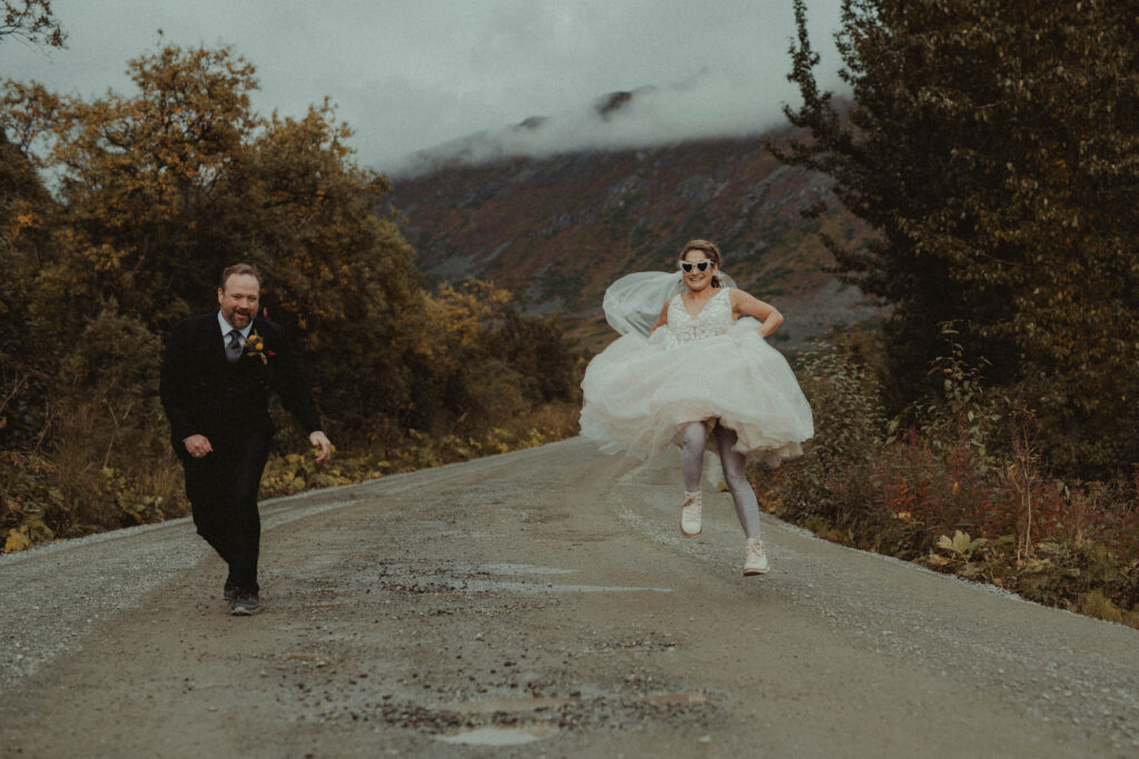 Bride and groom jump over puddles on a remote mountain road