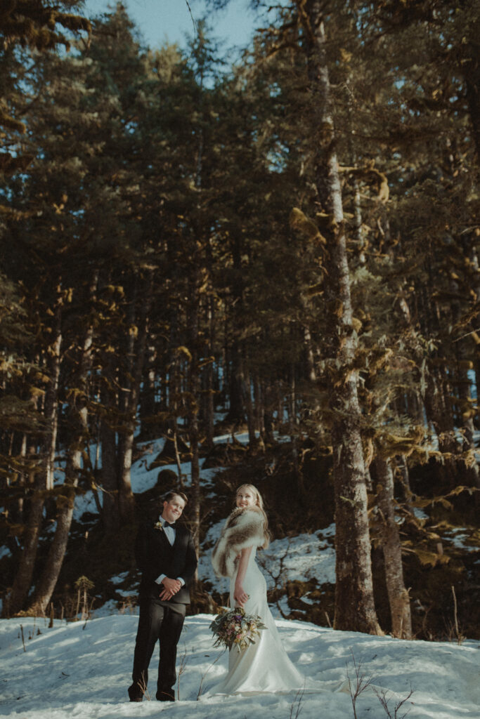 Bride and groom stand in a forest off the coast of seward, alaska