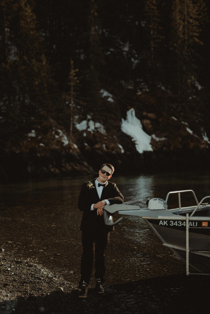 Groom stands with the bow of the boat on the shore of a remote beach in alaska