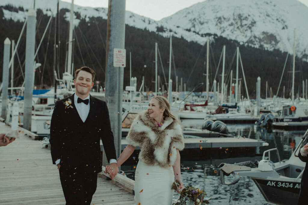 Couple walks hand in hand through a petal toss on the docks of the harbor in seward, alaska