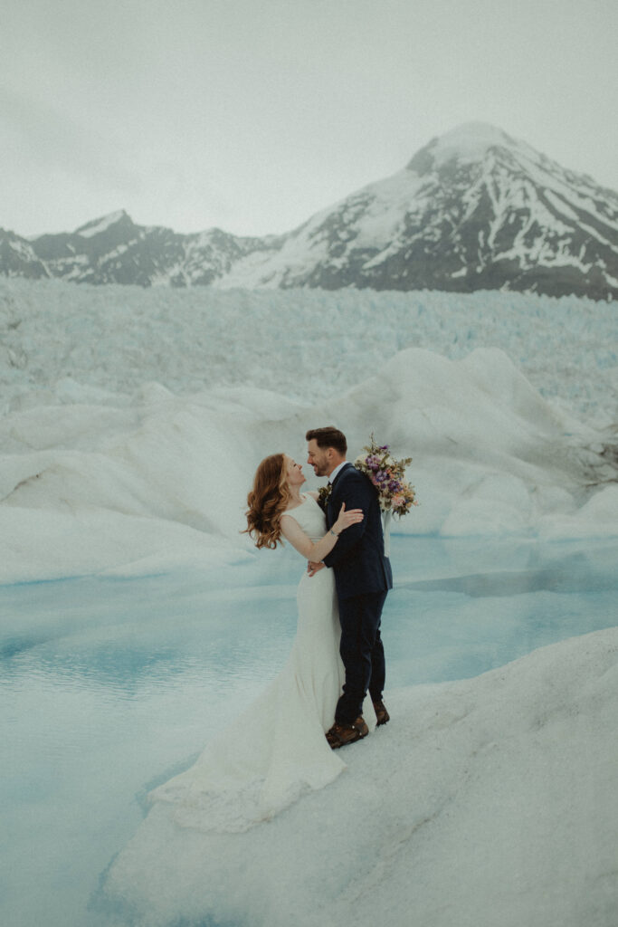 Bride and groom hug in front of a blue glacier pool