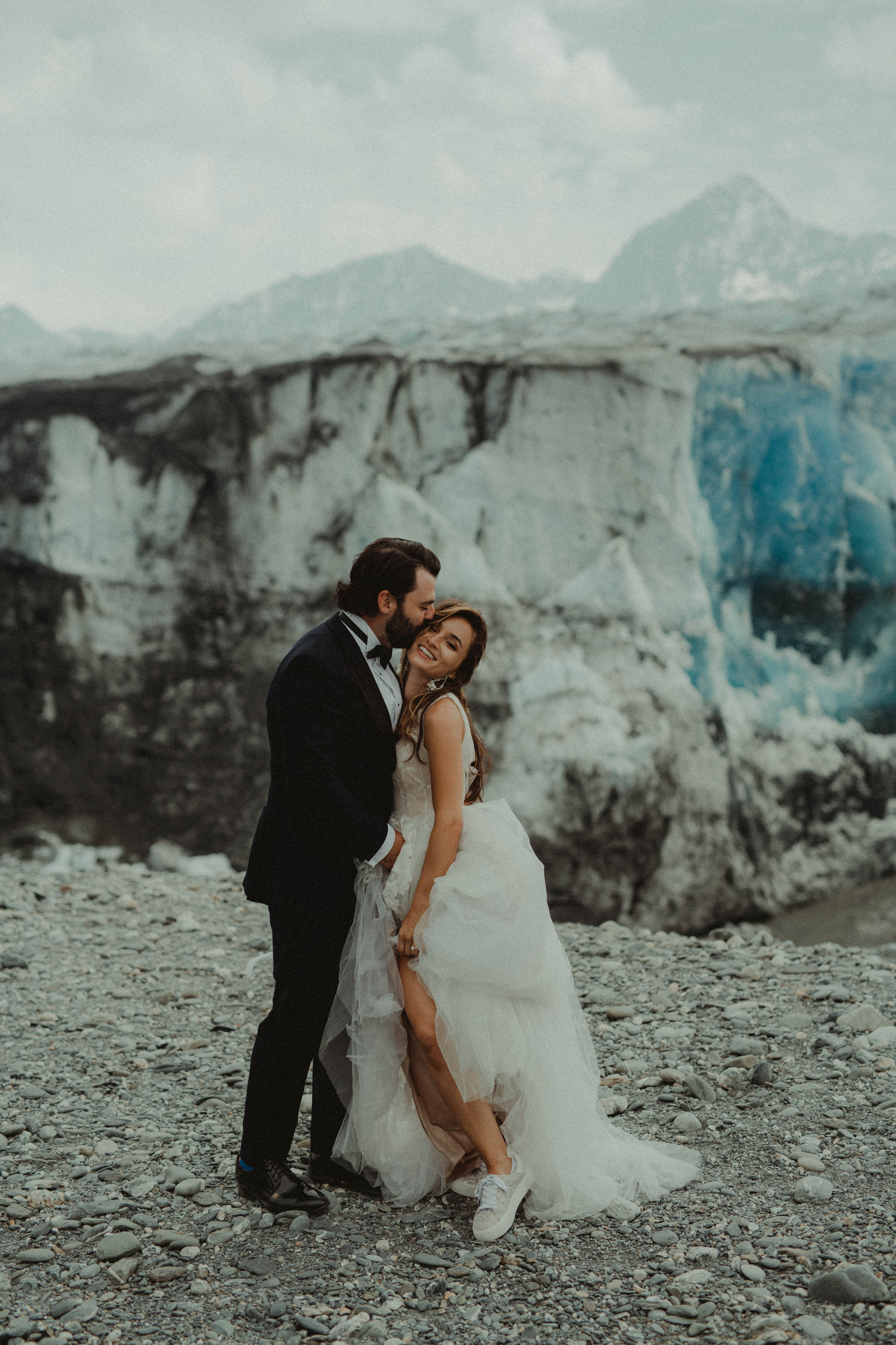 Bride and groom pose in front of a blue ice wall at knik glacier in Alaska