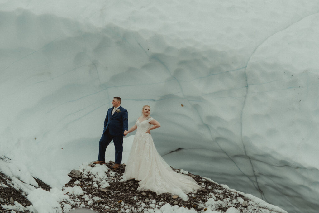 a bride and groom stand on a large piece of ice at Matanuska glacier