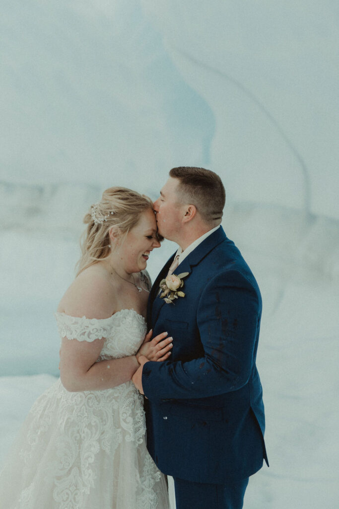 groom kissing the bride on the forehead at their epic alaskan elopement 