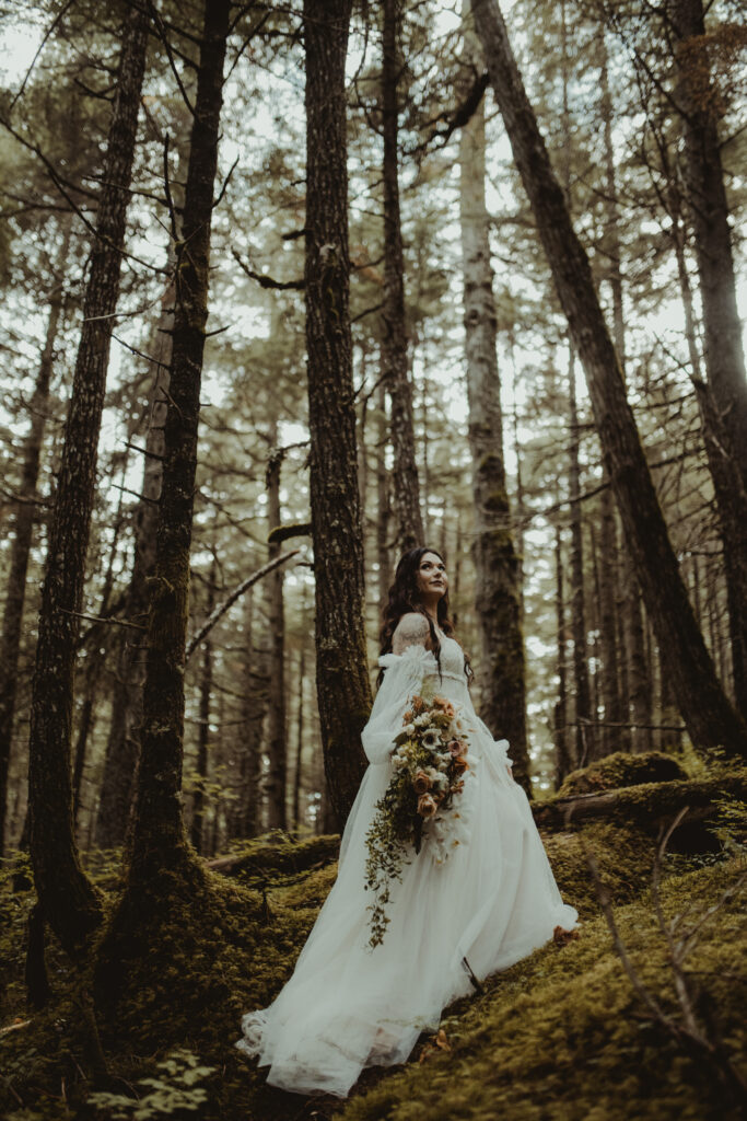 Bride poses in a forest in girdwood alaska holding a beautiful bridal bouquet 
