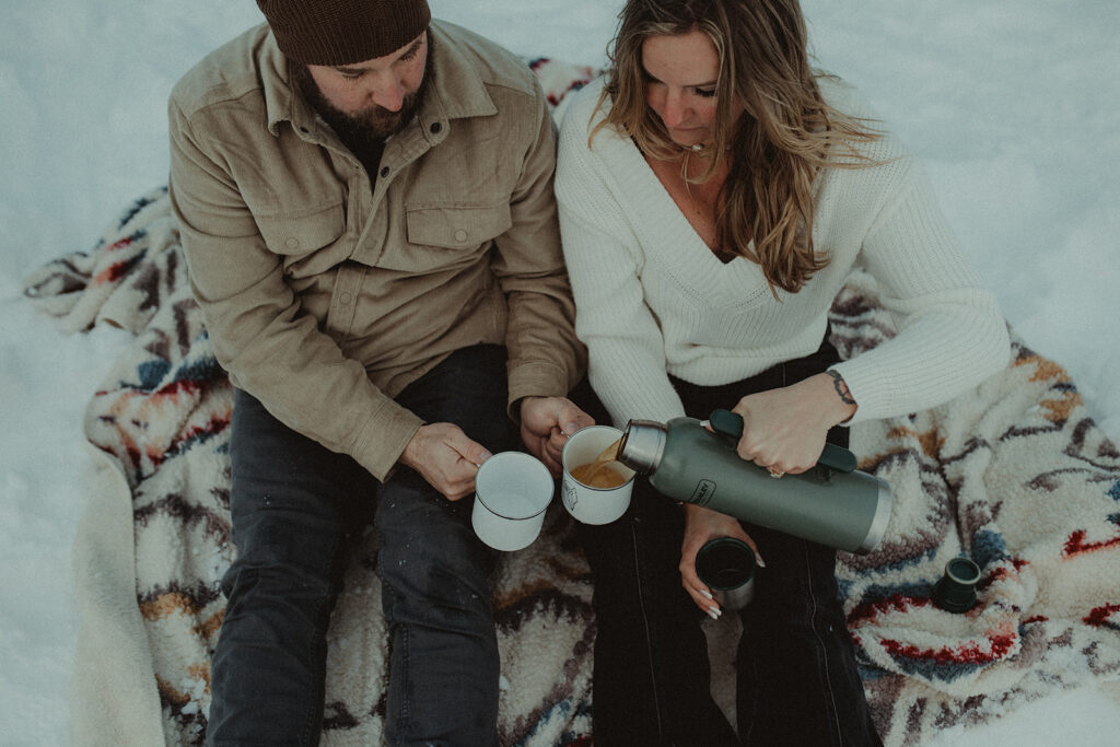 couple drinking coffee during their winter engagement photoshoot