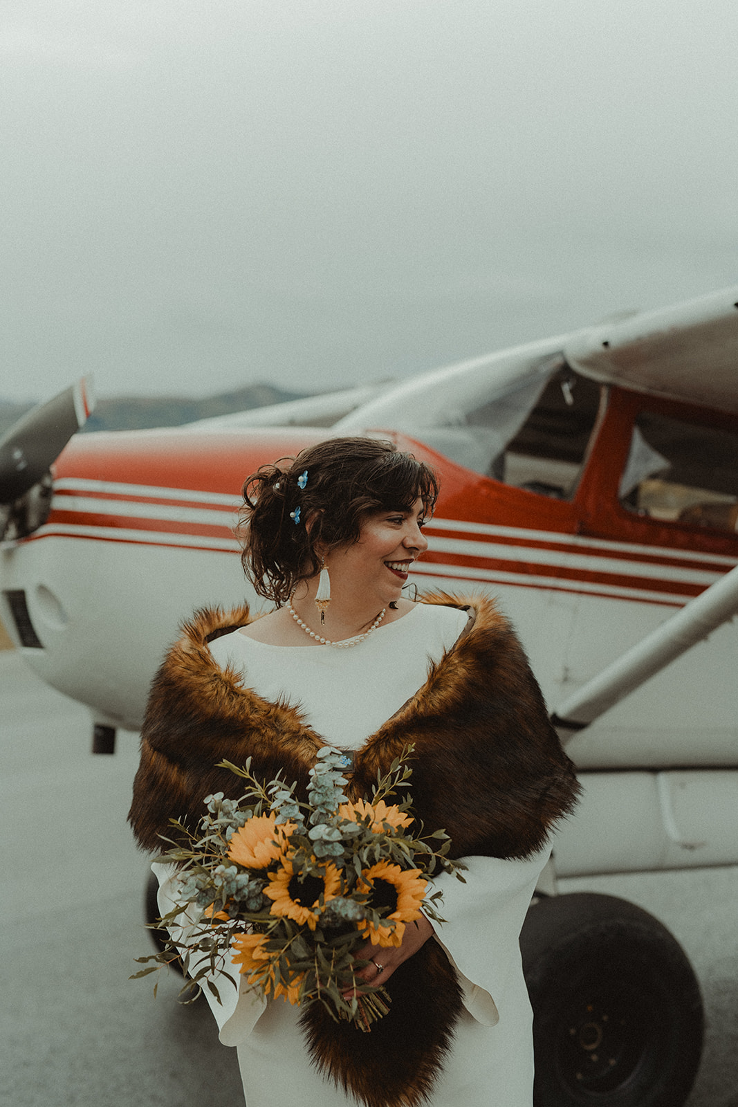 Bride stands in front of a bush plane with her bouquet of sunflowers